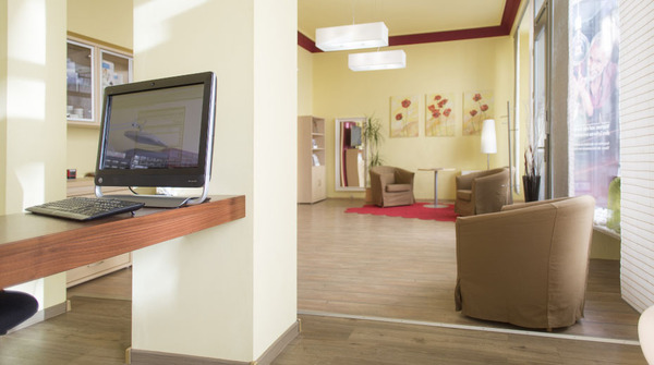 Modernes, helles Büro mit Computerarbeitsplatz und gemütlicher Sitzecke im Wartebereich.